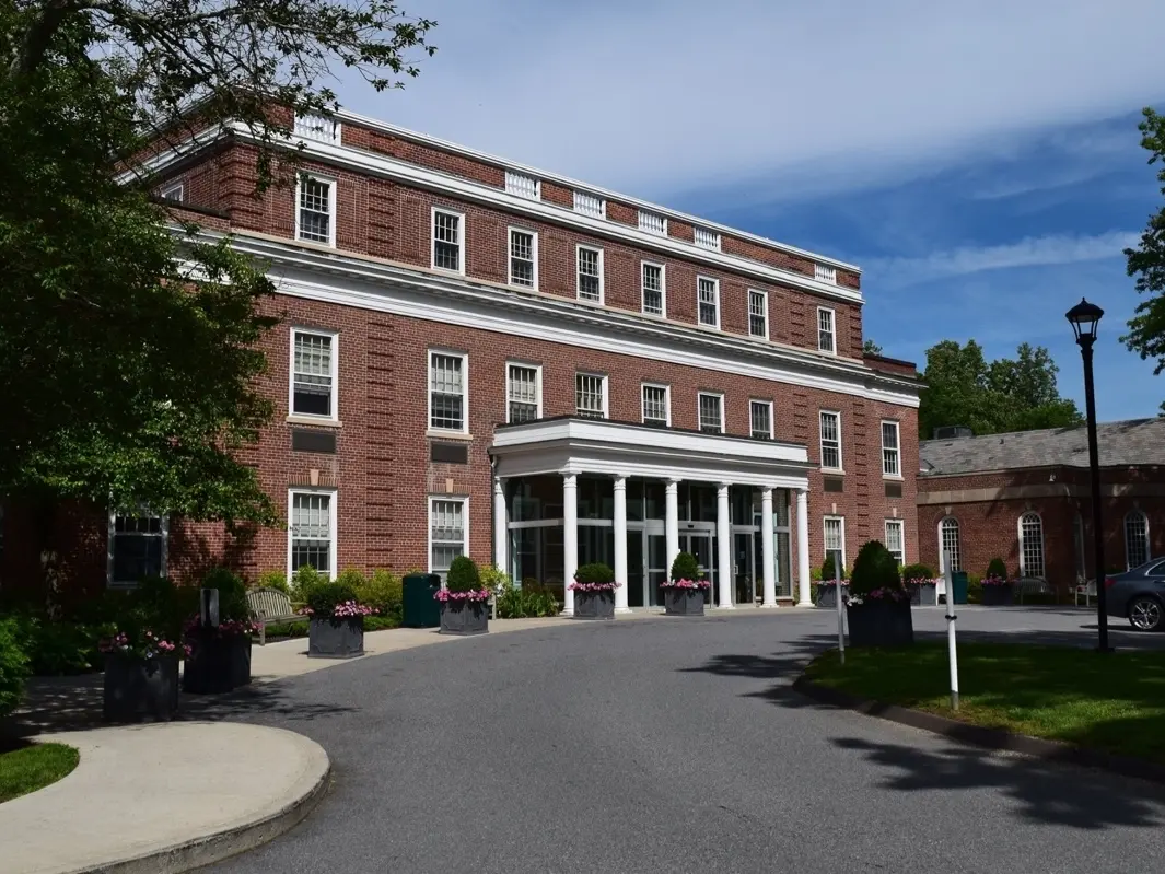 A brick building with a prominent entrance, surrounded by trees and landscaping under a clear sky.