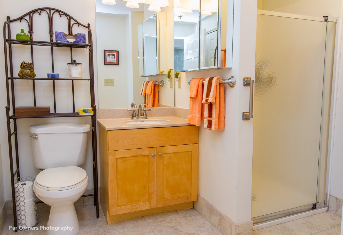 A cozy bathroom with a wooden vanity, mirror, orange towels, and a glass shower.