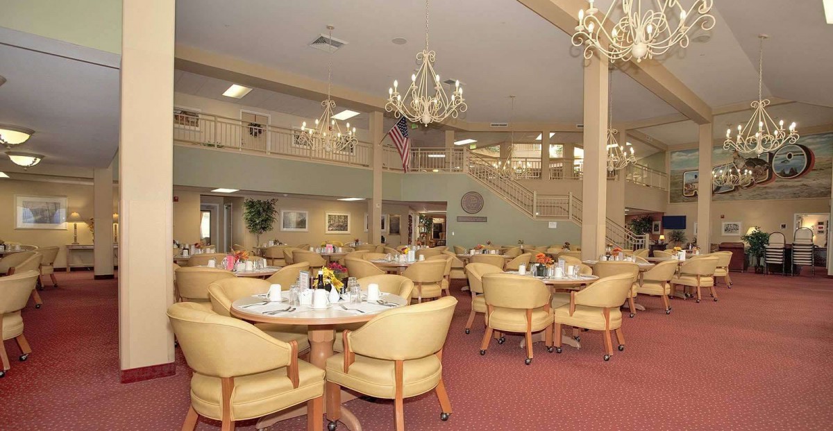 A spacious dining hall with elegant chandeliers, tables, and chairs arranged neatly.