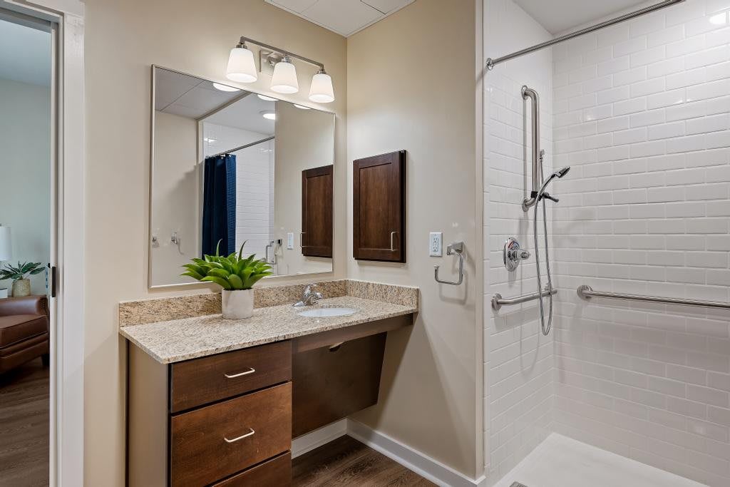 A modern bathroom with a wooden vanity, mirror, and a walk-in shower.