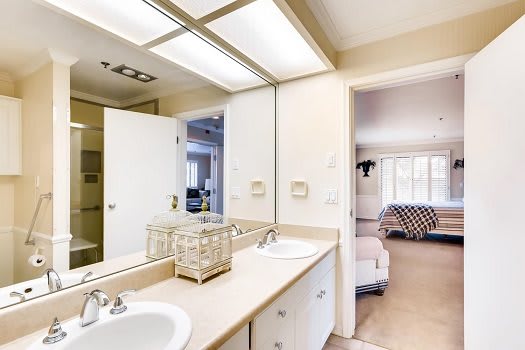 A modern bathroom featuring a double sink vanity with ample lighting and a view into an adjacent room.