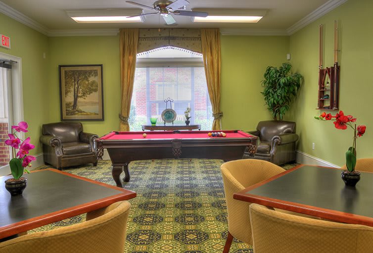 A cozy billiards room featuring a red pool table, surrounded by comfortable leather chairs and tasteful decor.