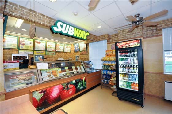 Interior of a Subway restaurant with a counter and beverage cooler.