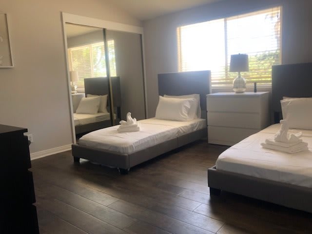 A minimalist bedroom with two twin beds, a large mirrored closet, and a nightstand with a lamp.