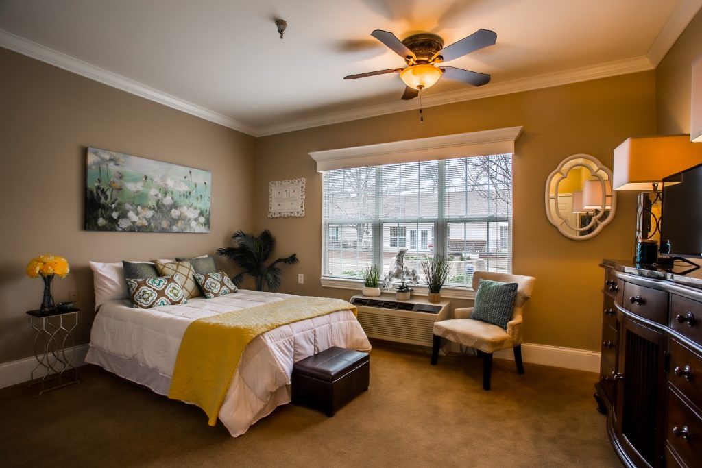 A cozy bedroom with a ceiling fan, artwork on the wall, and a large window allowing natural light to brighten the space.