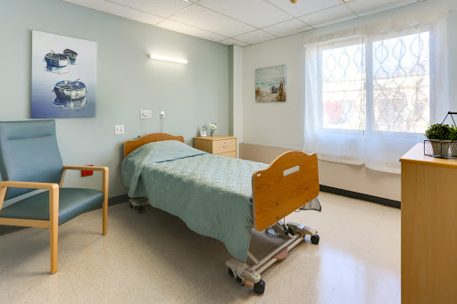 A well-lit and clean hospital patient room featuring a bed, chair, and soft-colored walls.