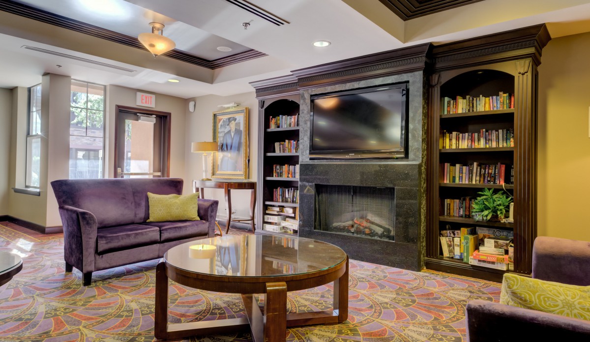 A cozy living room featuring a fireplace, bookshelves, and a television above a modern coffee table.