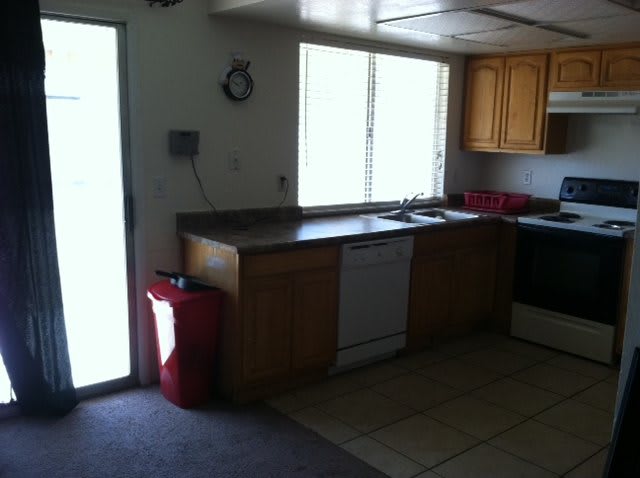 A kitchen interior featuring wooden cabinets, a dishwasher, stove, and a window allowing natural light.