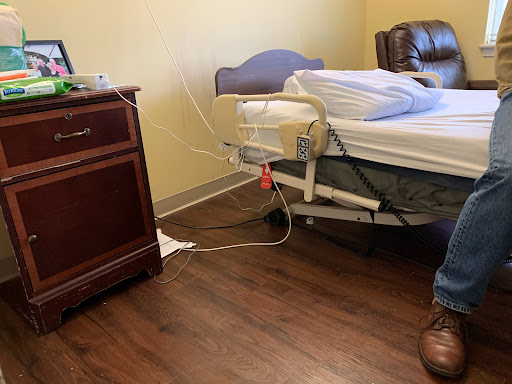A view of a hospital patient room featuring a bed, wooden furniture, and some medical equipment.