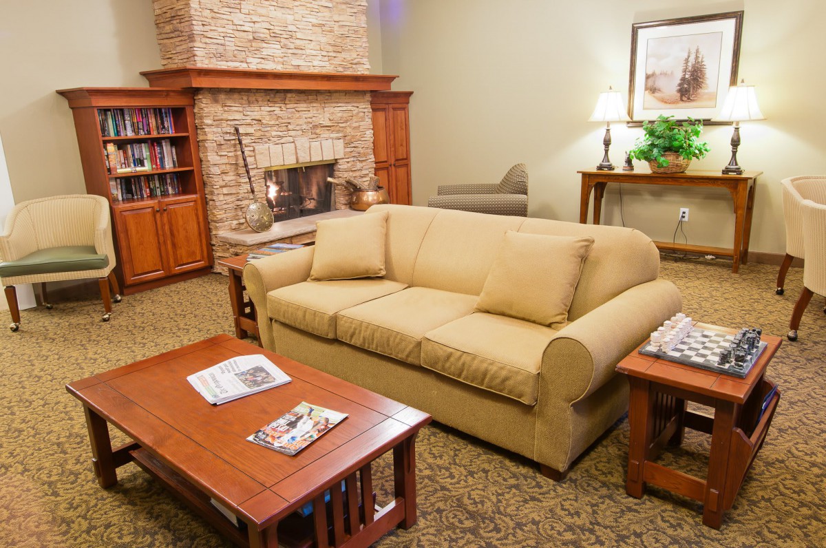 A cozy living room with a beige sofa, a wooden coffee table, a stone fireplace, and bookshelves.