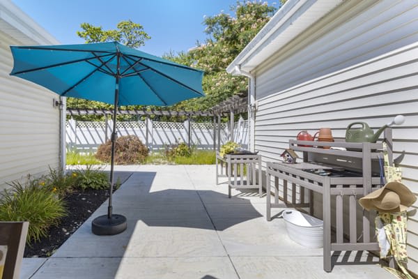 A sunny backyard patio with a blue umbrella and grill.