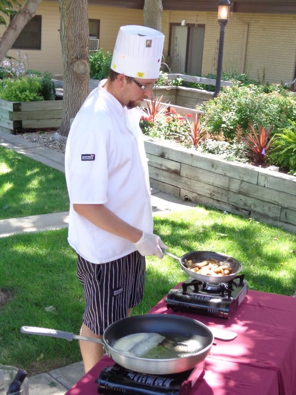 A chef cooking outdoors, wearing a white uniform and hat.