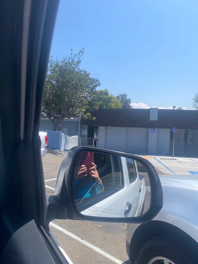 Reflection in a car side mirror showing a person taking a photo in a parking lot on a sunny day.