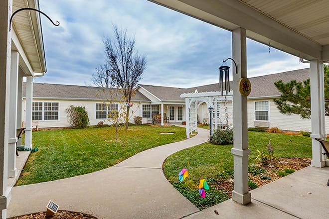 A serene courtyard featuring a winding pathway leading through a manicured garden, surrounded by a building with a welcoming front porch.