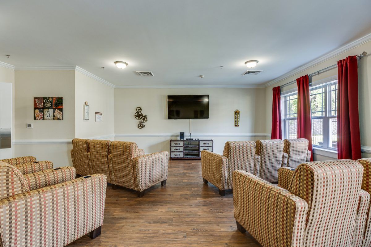 A cozy living room with multiple armchairs facing a television, featuring wood flooring and red curtains.