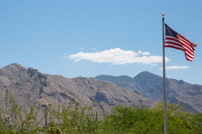 A scenic view of mountains with a clear blue sky and an American flag waving in the foreground.
