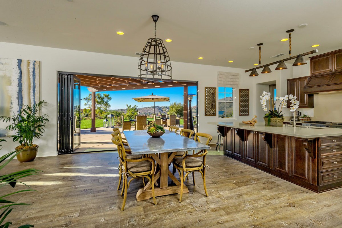 A modern open-plan dining room and kitchen with a seamless transition to an outdoor patio area, featuring wooden flooring and elegant decor.