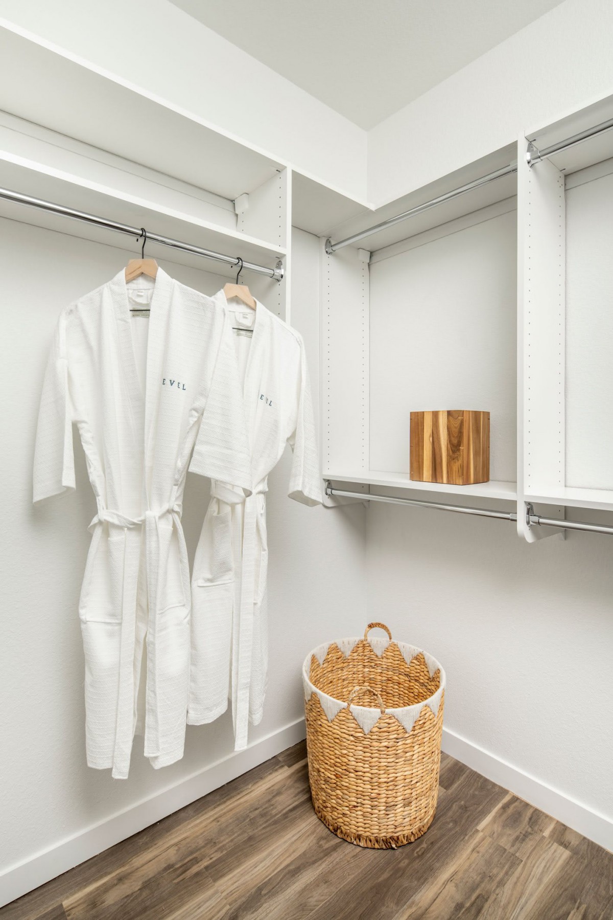 A neatly organized closet with white bathrobes, a wicker basket, and minimalist design.