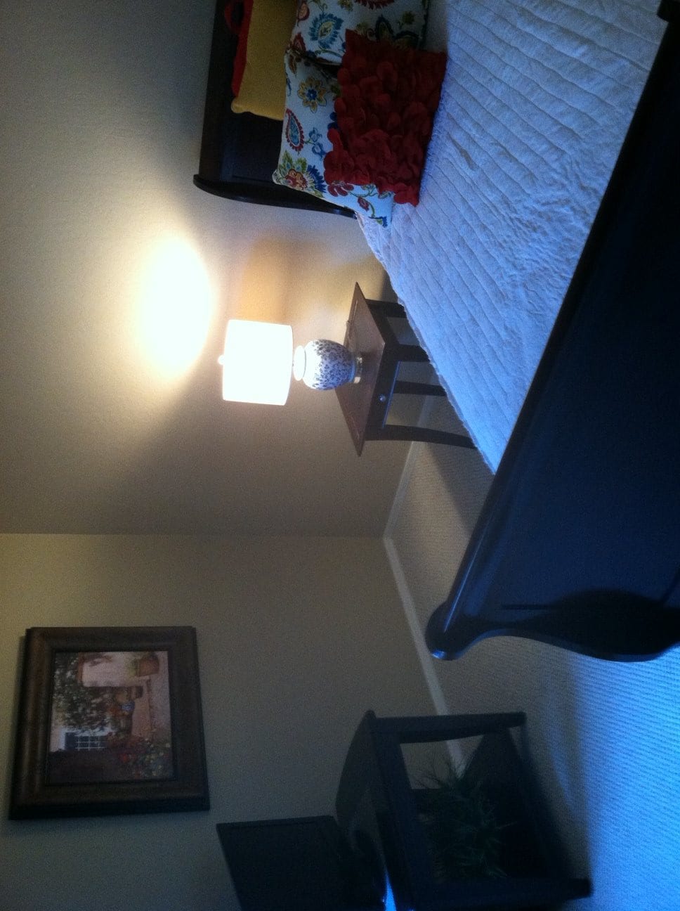 A cozy bedroom featuring a bed with a nightstand and lamp, accentuated by warm lighting and wall art.
