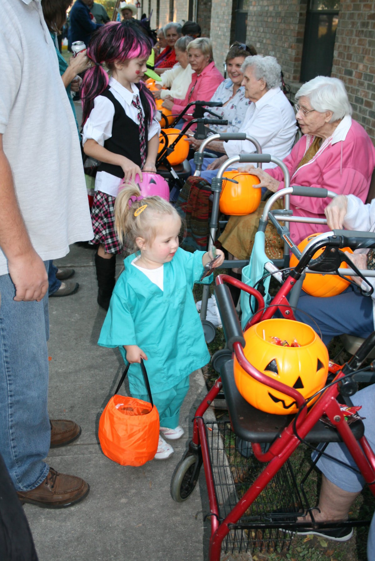 A young child dressed in a Halloween costume collects treats from elderly residents at a nursing home.