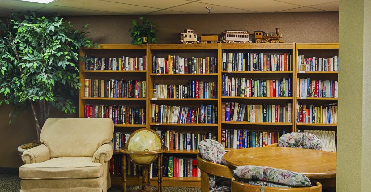 A cozy library space featuring bookshelves filled with books, an armchair, a globe, and a wooden table.