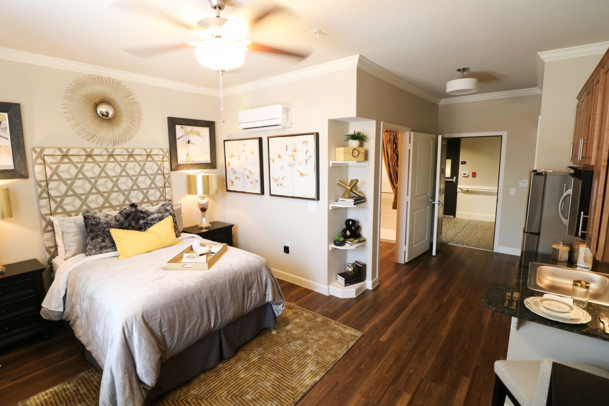 A modern and stylish bedroom with wooden flooring, featuring a neatly made bed, decorative wall art, open shelving, and a ceiling fan.