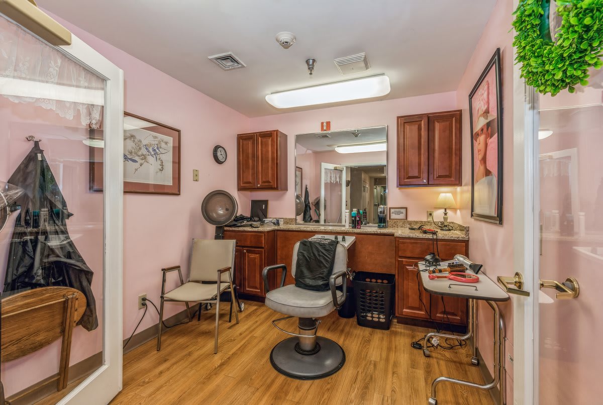 Interior of a cozy hair salon with a central chair, wooden cabinets, and a large mirror.