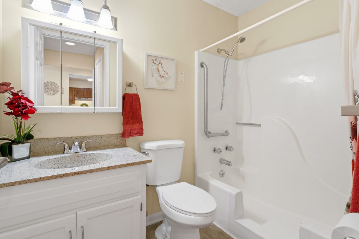 A clean and modern bathroom featuring a shower, toilet, sink, and mirror with a red towel for accent.