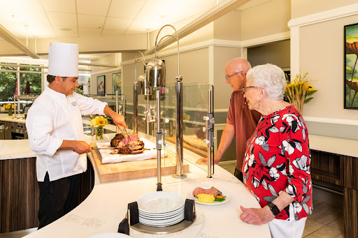 A chef serves freshly carved meat at a buffet while two customers watch eagerly.