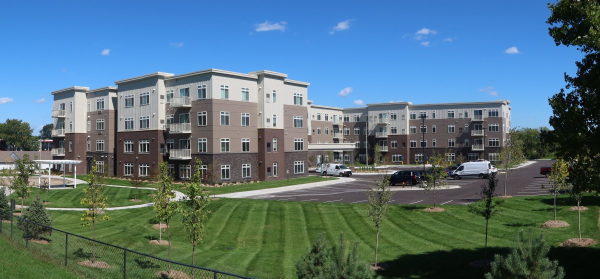 A modern apartment complex with well-maintained landscaping under a clear blue sky.