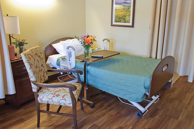 A hospital room with a patient bed, chair, and tray table adorned with flowers.