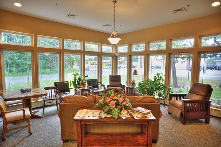 A cozy living room with large windows, featuring comfortable seating and indoor plants.