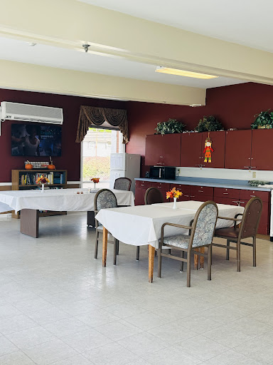 A spacious dining area with tables and chairs, featuring a kitchenette against red walls.