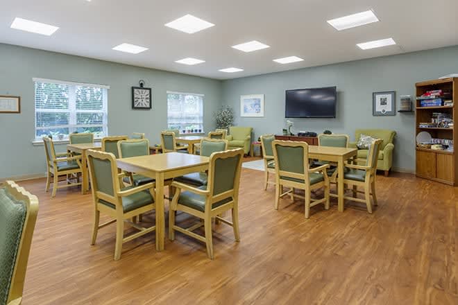 A spacious meeting room with multiple tables and chairs, featuring a television on the wall.