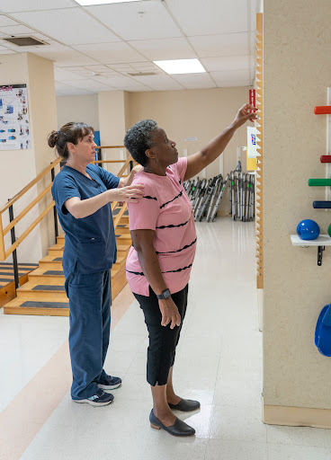 A physical therapist assists a patient in reaching for an object as part of a rehabilitation exercise.