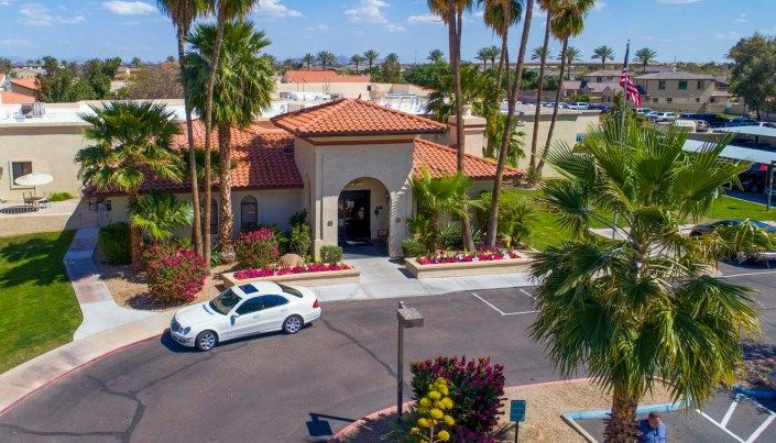 A scenic view of a tropical building with a car parked in the driveway, surrounded by palm trees.
