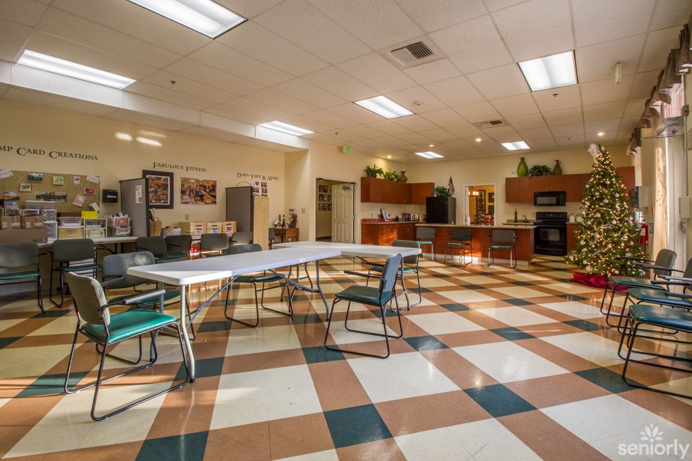 A spacious community room with a kitchen, featuring tables and chairs on a checkered floor.
