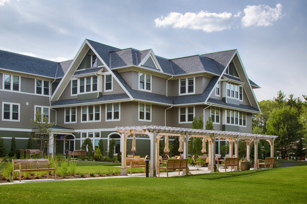 A beautiful multi-story residential house with a well-kept garden and pergola.