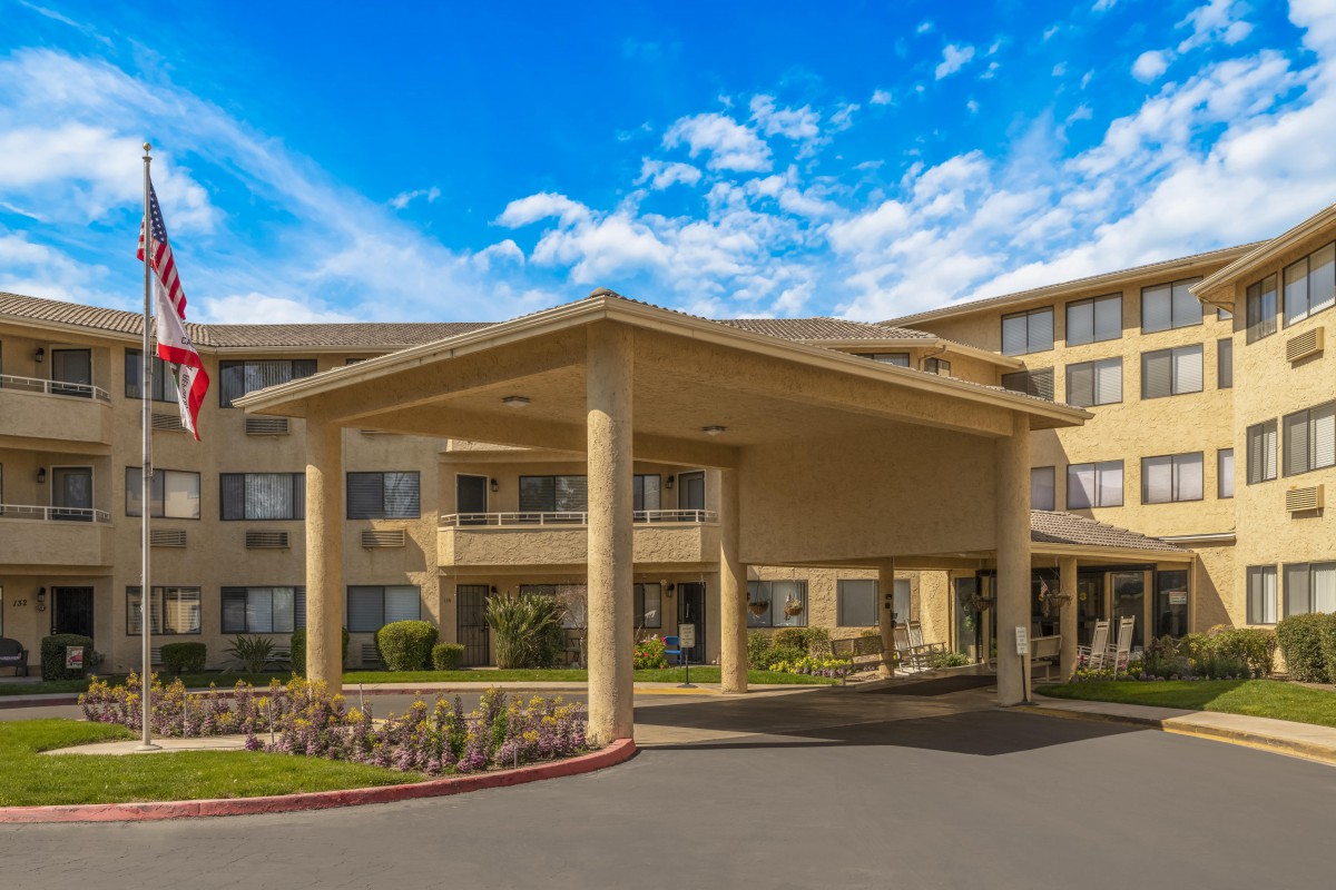 The exterior view of a hotel entrance with a covered driveway and landscaped surroundings on a clear day.