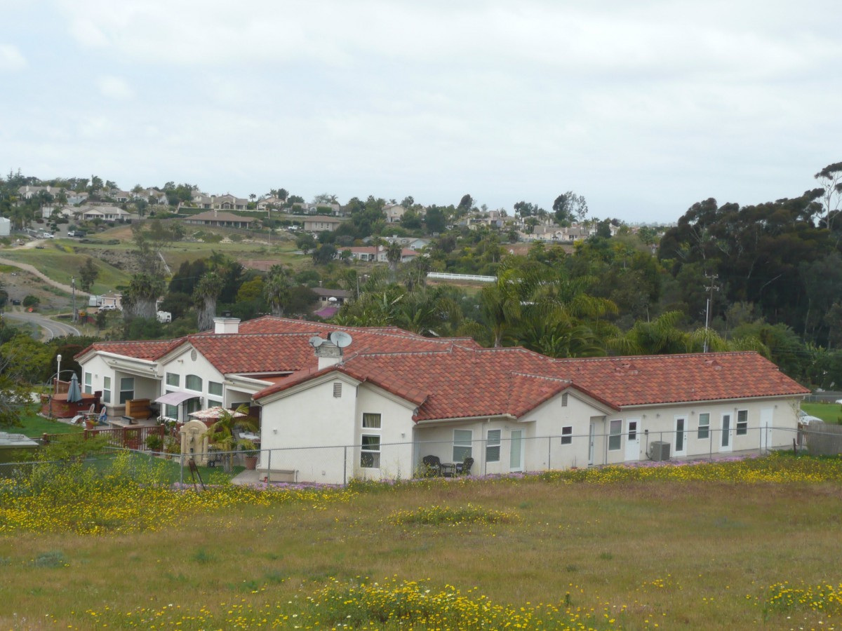 A view of a building with a red roof surrounded by grassy fields in a countryside setting.