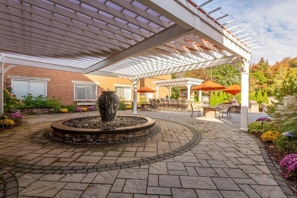 A beautifully designed outdoor patio with a fountain and seating area under a pergola.
