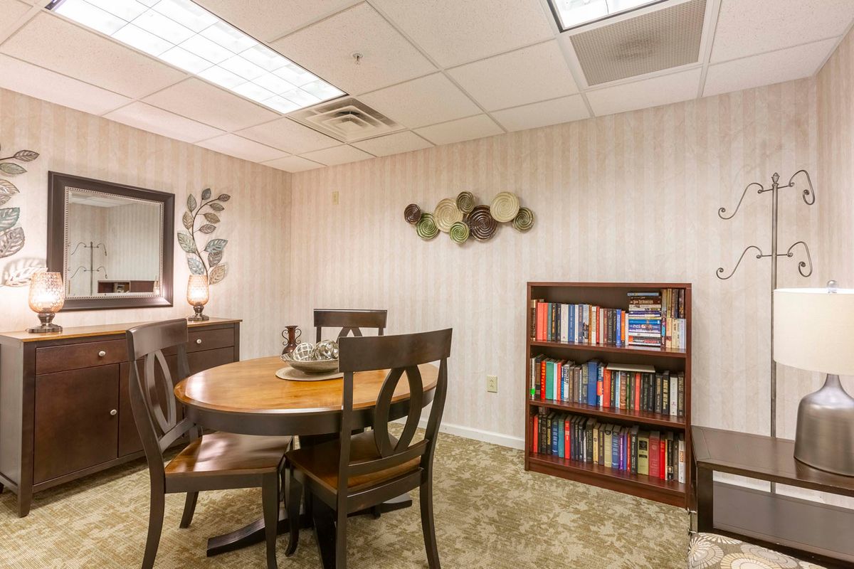 A cozy meeting room with a round table, chairs, and a bookshelf filled with books.