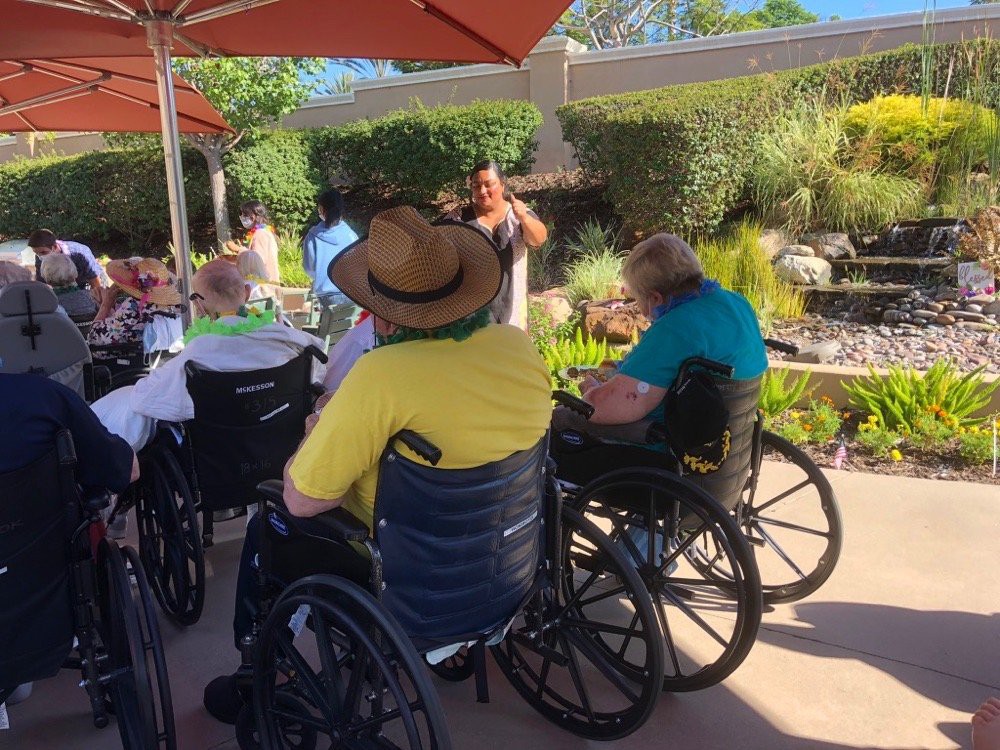 A group of people in wheelchairs enjoying a sunny day in a garden setting.