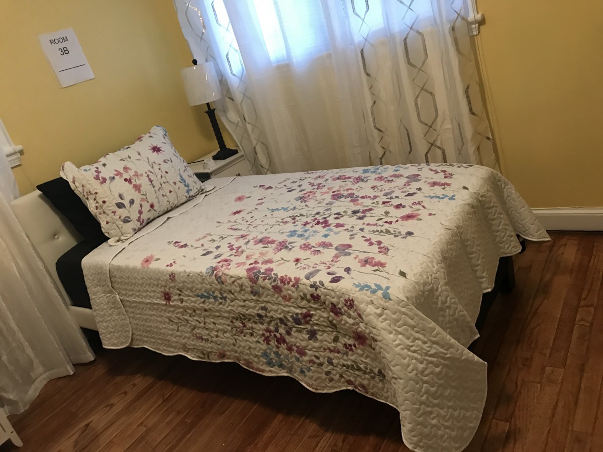 A cozy bedroom with a floral bedspread, wooden floor, and soft lighting.