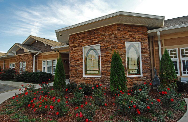 A house with a brick exterior and well-maintained landscaping featuring red flowers and green shrubs.