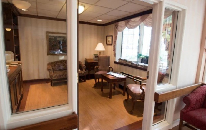 A cozy office space with a desk, chairs, and a lamp near a large window.
