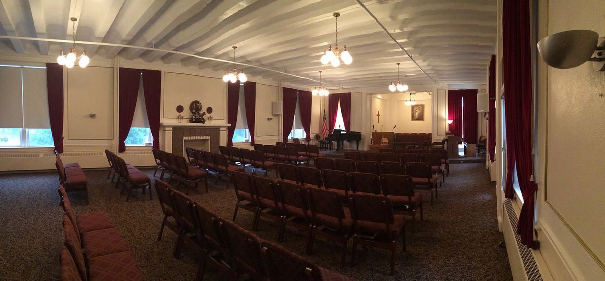 A historic auditorium with rows of wooden chairs and a piano under classic chandeliers.