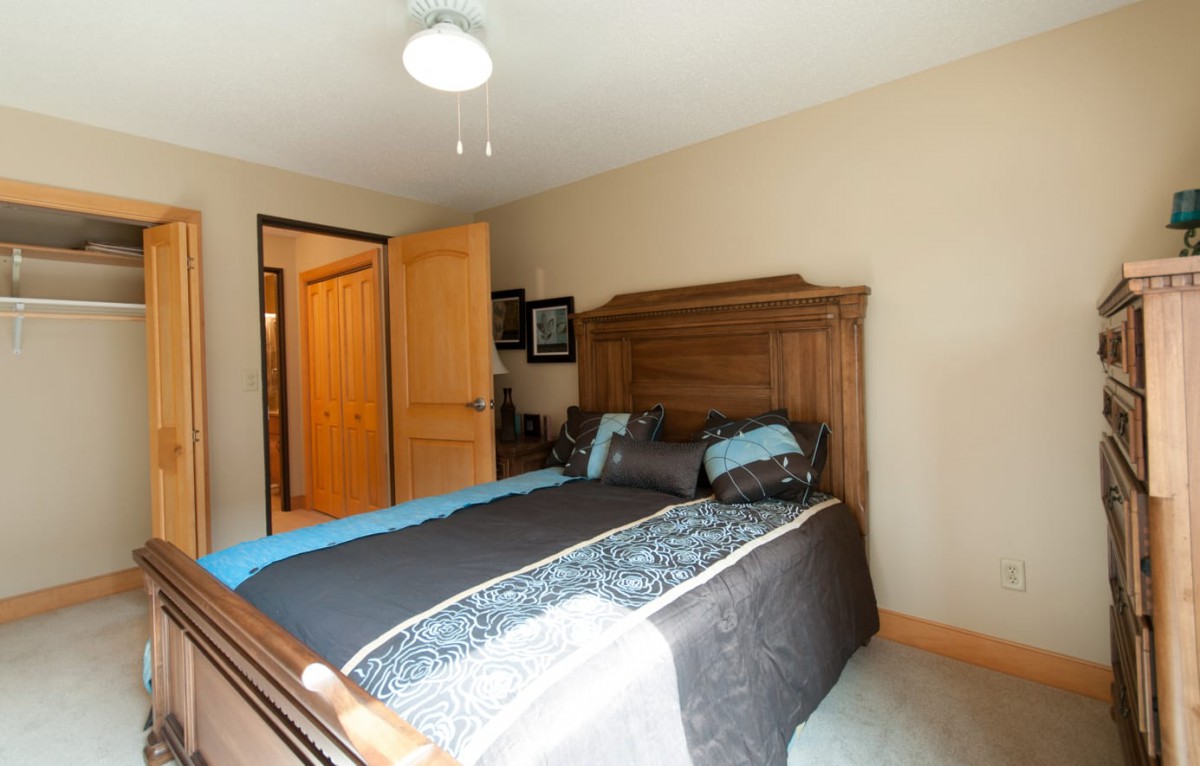 A cozy bedroom featuring a wooden bed frame with blue and gray bedding, enhanced by warm lighting and simple decor.