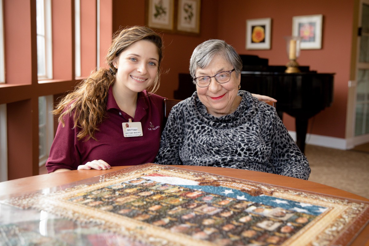A young woman and an elderly person sitting together, working on a puzzle indoors.