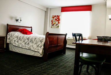 A cozy bedroom with a wooden bed, desk, and chair, featuring red accents.